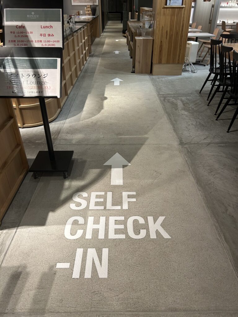 館内に入ると、床面に「セルフチェックイン」の文字と矢印表示がございます。 　矢印に沿って、チェックイン機までお進みください。